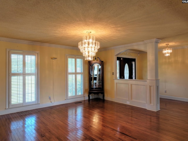 unfurnished dining area featuring crown molding, arched walkways, an inviting chandelier, baseboards, and wood-type flooring