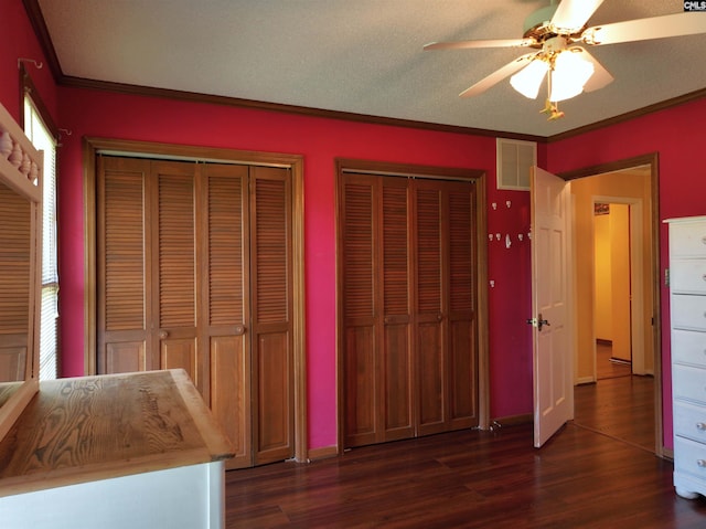 unfurnished bedroom with crown molding, visible vents, wood finished floors, and two closets