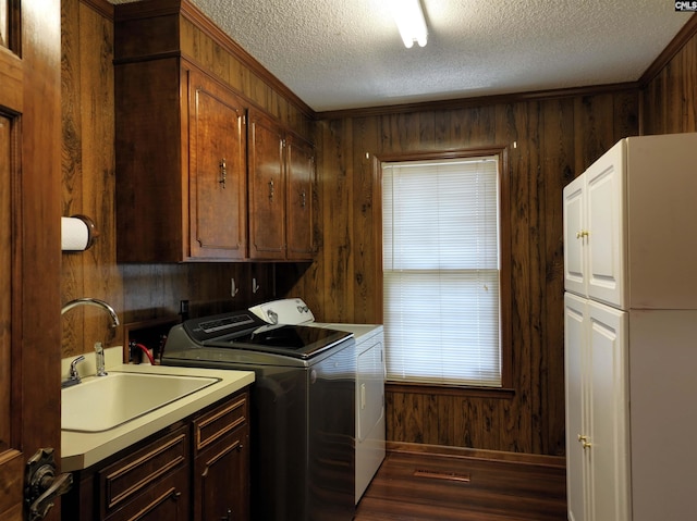 clothes washing area with a sink, cabinet space, washing machine and clothes dryer, a textured ceiling, and wood finished floors