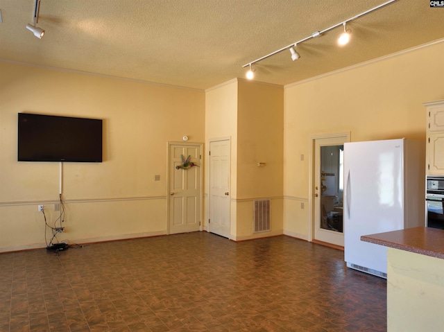 unfurnished living room featuring a textured ceiling, track lighting, and visible vents