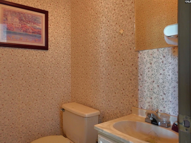 half bath with vanity, toilet, and wallpapered walls