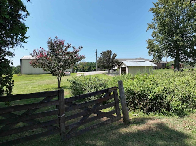view of gate with fence, an outdoor structure, a lawn, and an outbuilding