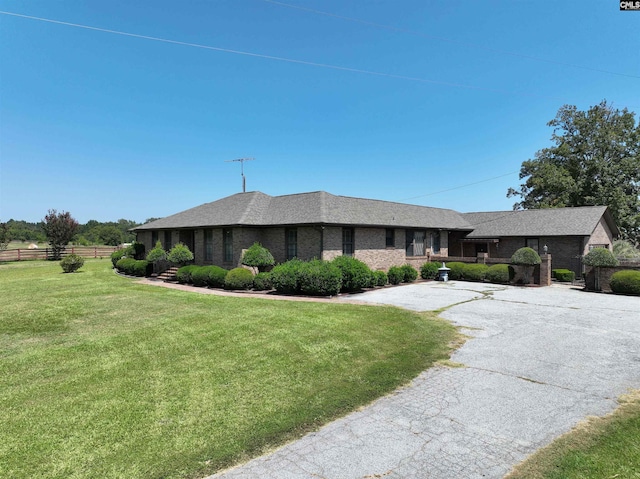 single story home featuring brick siding, fence, a front yard, and roof with shingles