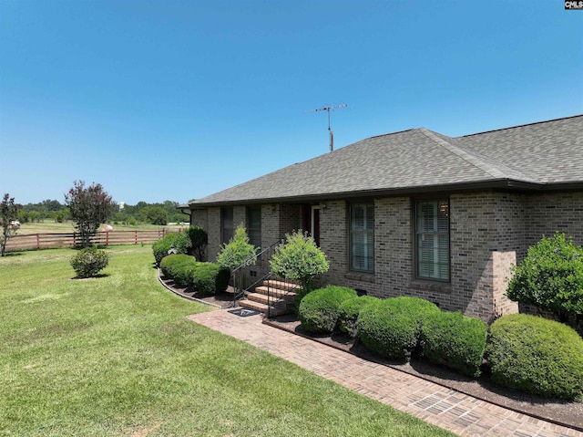 view of front facade featuring fence, roof with shingles, a front yard, and brick siding