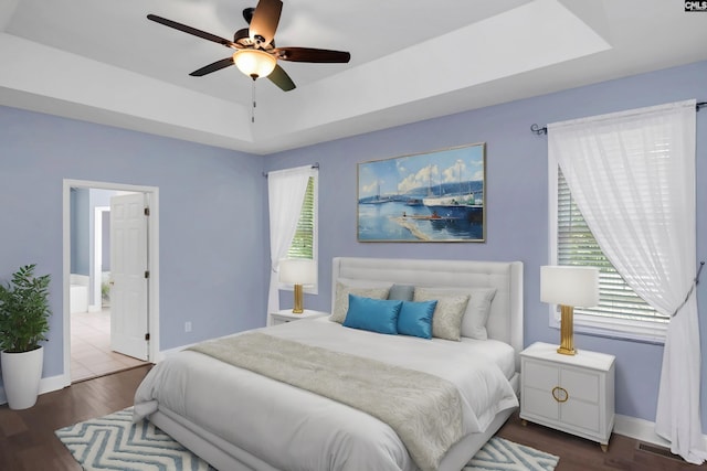 bedroom with a raised ceiling, ceiling fan, hardwood / wood-style floors, and ensuite bath