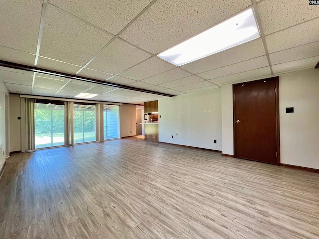 empty room featuring light wood-style floors, floor to ceiling windows, baseboards, and a drop ceiling