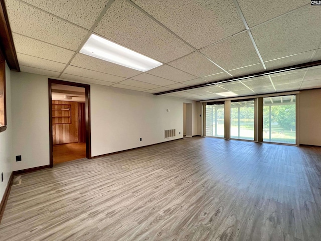 unfurnished room featuring a paneled ceiling, wood finished floors, visible vents, baseboards, and a wall of windows