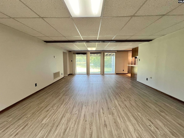 interior space with visible vents, a drop ceiling, baseboards, and wood finished floors