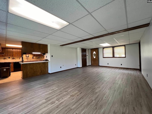 unfurnished living room featuring wood finished floors, a paneled ceiling, and baseboards