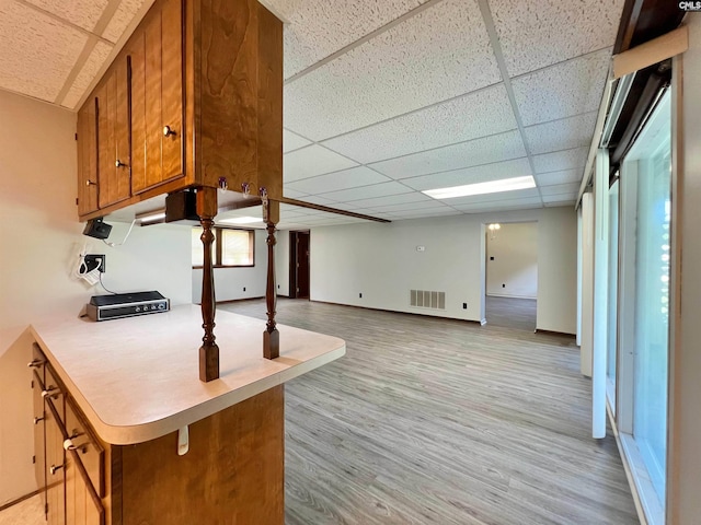 kitchen with light countertops, visible vents, brown cabinetry, light wood-type flooring, and a drop ceiling