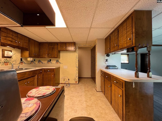 kitchen featuring brown cabinets, light countertops, a sink, and a peninsula