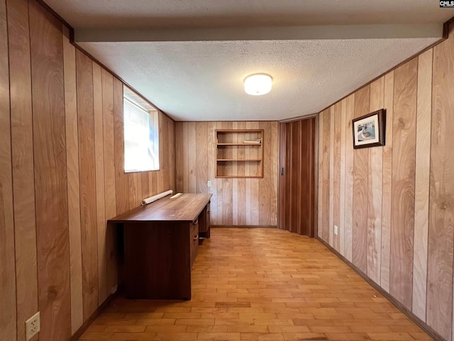 unfurnished office featuring light wood-style floors, wood walls, and a textured ceiling