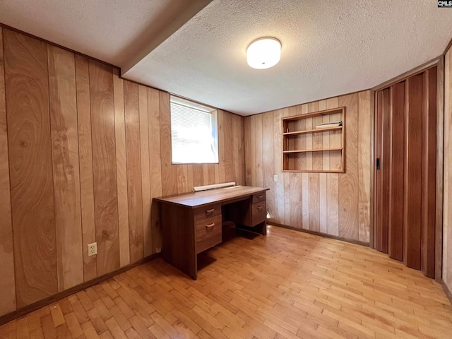 unfurnished office featuring a textured ceiling, built in features, light wood-style flooring, and wooden walls