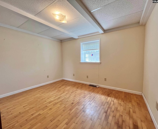 spare room featuring a paneled ceiling, light wood finished floors, and baseboards