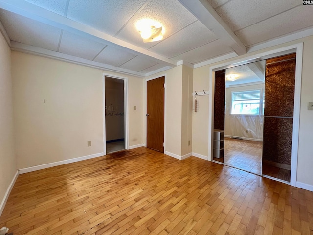 unfurnished bedroom featuring light wood finished floors, baseboards, and beamed ceiling