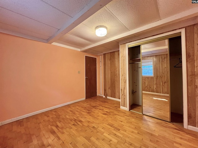 unfurnished bedroom featuring light wood-style floors, beamed ceiling, wooden walls, and baseboards