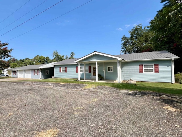 single story home featuring metal roof, a garage, covered porch, driveway, and a front yard