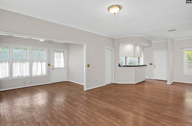 unfurnished living room with a wealth of natural light, dark wood-type flooring, and crown molding