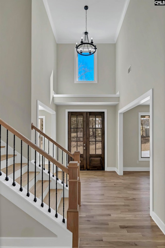 entrance foyer with light wood-type flooring, a high ceiling, french doors, ornamental molding, and a chandelier