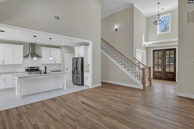 kitchen featuring appliances with stainless steel finishes, light hardwood / wood-style floors, wall chimney range hood, and white cabinets