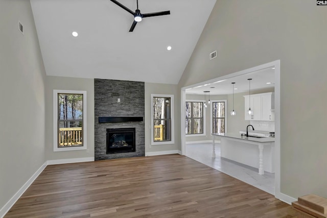 unfurnished living room featuring light hardwood / wood-style floors, high vaulted ceiling, a large fireplace, ceiling fan, and sink