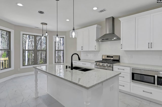 kitchen featuring pendant lighting, stainless steel appliances, a kitchen island with sink, sink, and wall chimney range hood