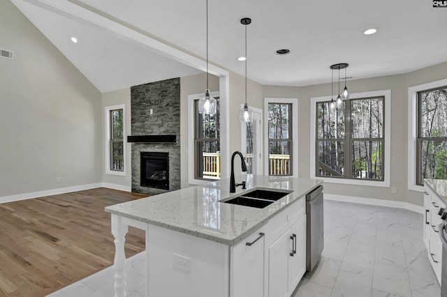 kitchen featuring an island with sink, light stone counters, white cabinets, a stone fireplace, and sink