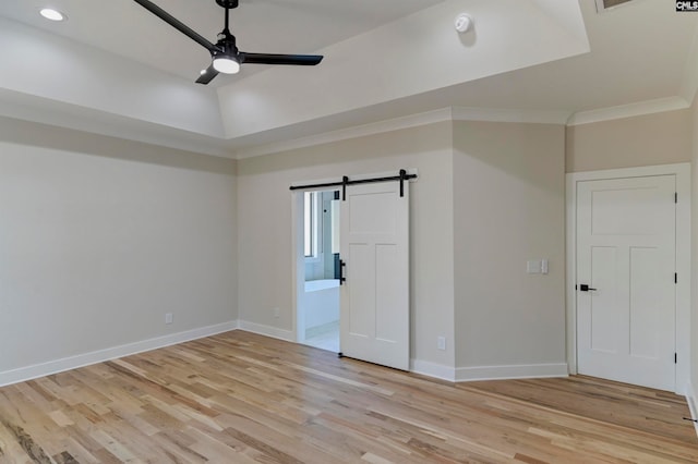 unfurnished bedroom with a barn door, light hardwood / wood-style flooring, ensuite bathroom, ornamental molding, and ceiling fan