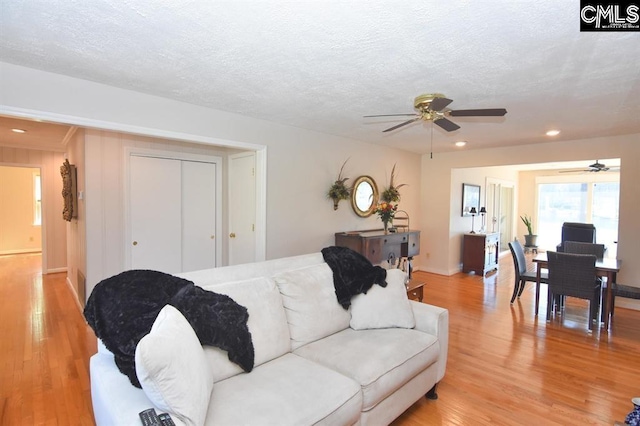 living room featuring ceiling fan, a textured ceiling, and light hardwood / wood-style flooring