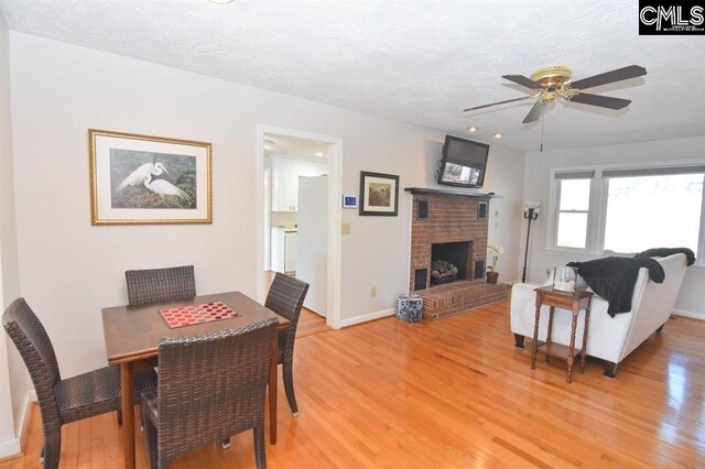 dining area with a textured ceiling, a brick fireplace, ceiling fan, and light hardwood / wood-style floors