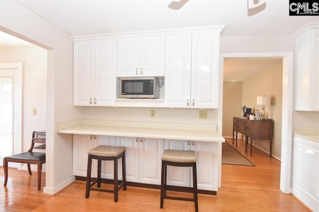 kitchen with light hardwood / wood-style flooring, ceiling fan, a kitchen breakfast bar, and white cabinetry