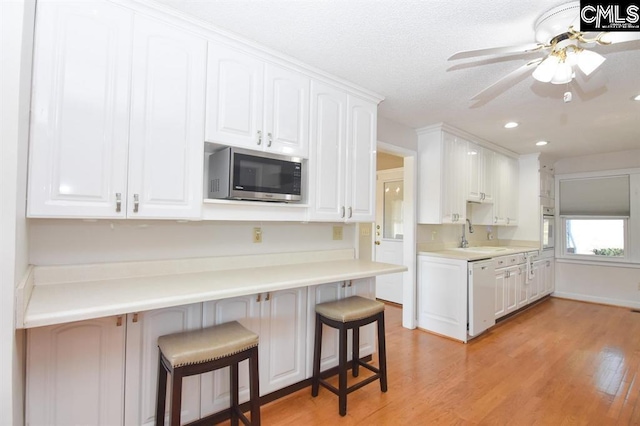 kitchen featuring a kitchen breakfast bar, white appliances, light hardwood / wood-style flooring, ceiling fan, and white cabinets