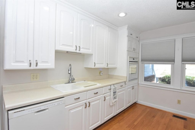 kitchen with a textured ceiling, white appliances, sink, white cabinetry, and light wood-type flooring