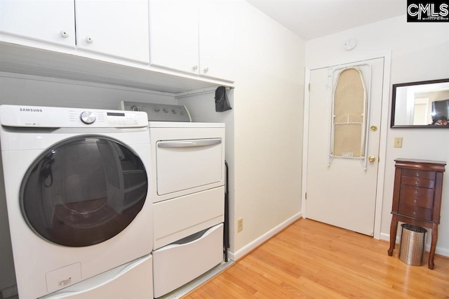 clothes washing area with cabinets, washing machine and dryer, and light hardwood / wood-style floors