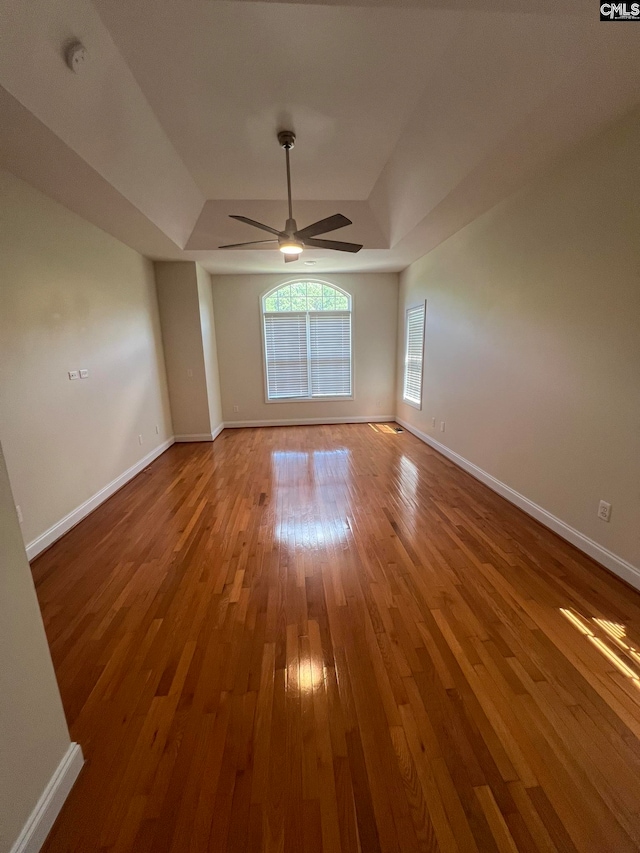 empty room with a tray ceiling, hardwood / wood-style floors, and ceiling fan