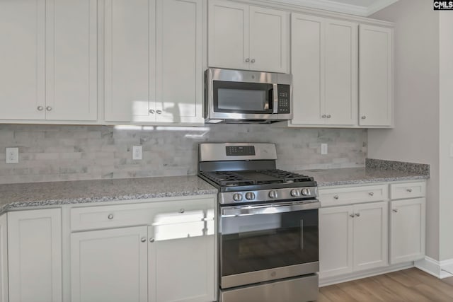 kitchen with light wood-type flooring, tasteful backsplash, light stone countertops, appliances with stainless steel finishes, and white cabinets