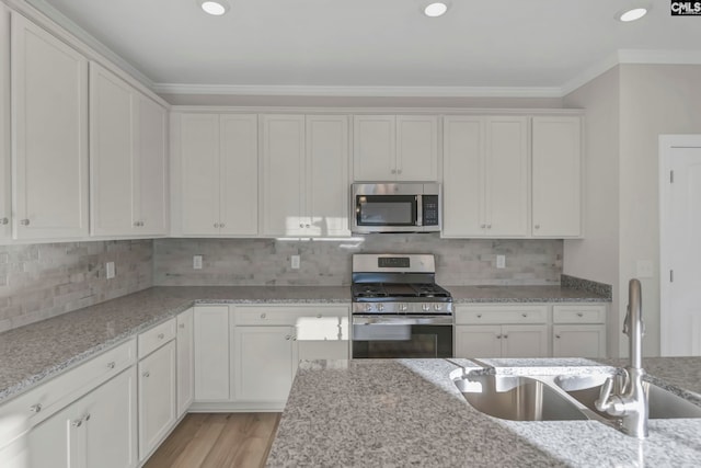 kitchen with white cabinets, light wood-type flooring, appliances with stainless steel finishes, sink, and decorative backsplash