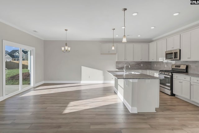 kitchen with a center island with sink, backsplash, appliances with stainless steel finishes, white cabinetry, and light stone counters