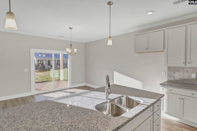 kitchen with light hardwood / wood-style flooring, light stone counters, sink, and decorative light fixtures