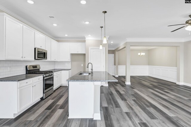 kitchen featuring dark stone countertops, ceiling fan with notable chandelier, stainless steel appliances, sink, and a center island with sink