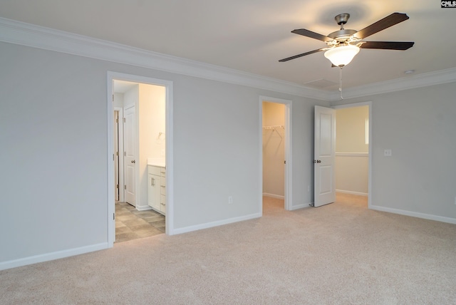 unfurnished bedroom featuring a spacious closet, ceiling fan, crown molding, ensuite bathroom, and light carpet