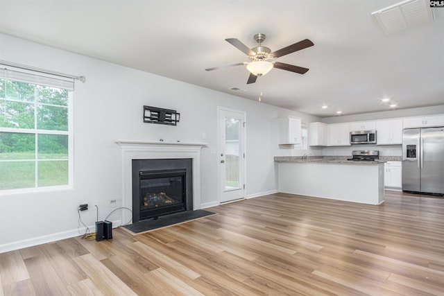 unfurnished living room featuring plenty of natural light, ceiling fan, and light wood-type flooring