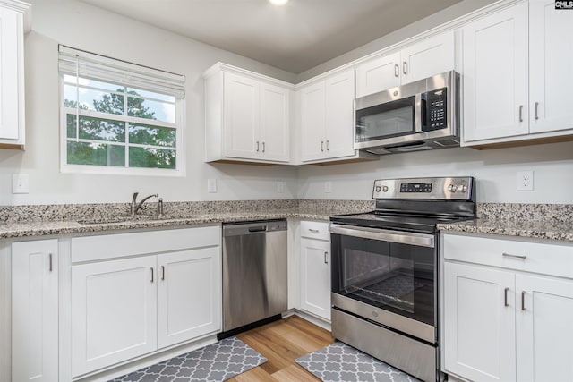 kitchen featuring light hardwood / wood-style flooring, light stone counters, stainless steel appliances, white cabinetry, and sink