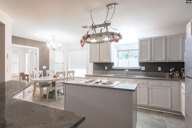 kitchen featuring hanging light fixtures, white cabinetry, a center island, sink, and a chandelier