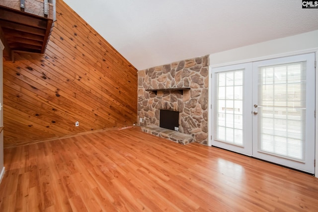 unfurnished living room with a healthy amount of sunlight, wood walls, and a stone fireplace