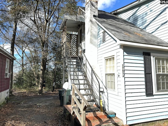 view of side of home with stairway, cooling unit, a chimney, and a shingled roof