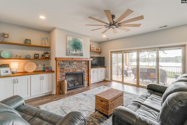 living room featuring ceiling fan, light hardwood / wood-style floors, and a stone fireplace