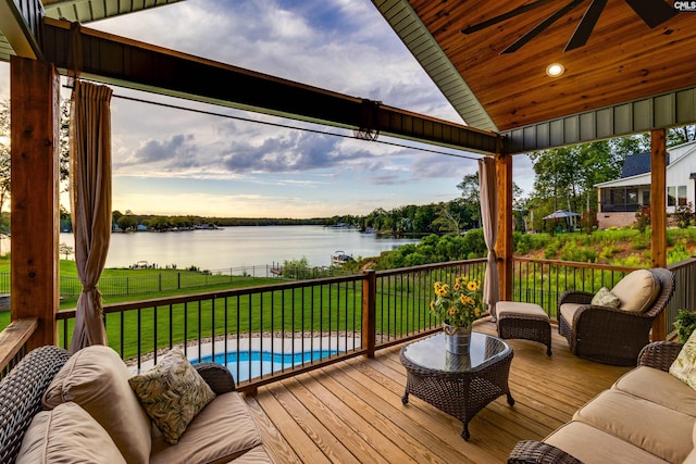 deck at dusk with an outdoor hangout area, a water view, a yard, ceiling fan, and a fenced in pool