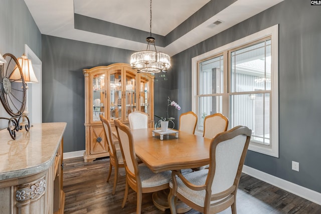 dining space featuring a tray ceiling, an inviting chandelier, and dark hardwood / wood-style floors