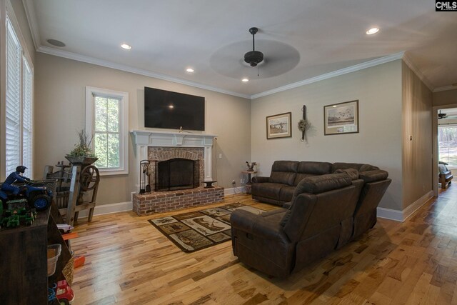 living room with light wood-type flooring, crown molding, a brick fireplace, and ceiling fan